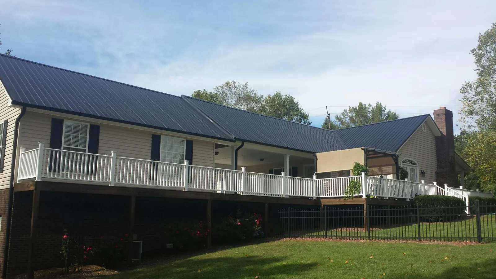 Black metal roof above a long white railed deck on a hillside home in Union